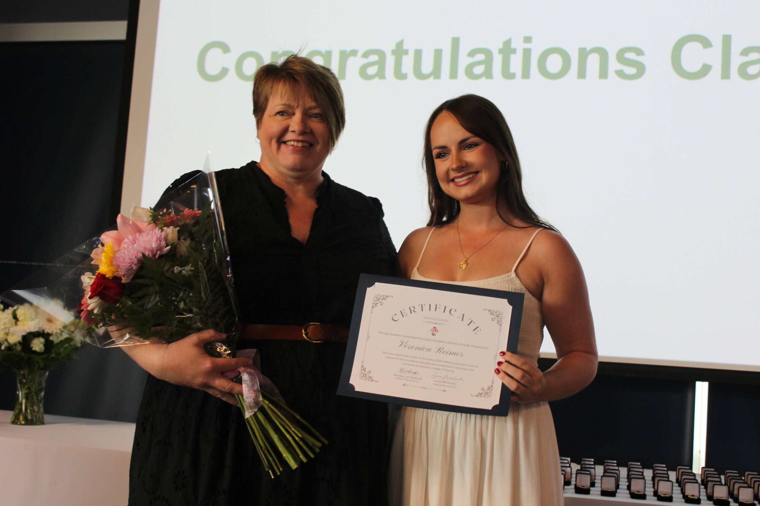 Veronica Reimer holding a certificate standing beside an individual holding flowers